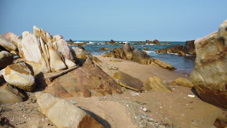 Sandy-beach-with-rocks-polluted-with-washed-out-rubbish,-low-altitude-gimbal
