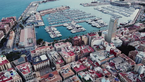 Alicante,-Spain,-Aerial-View-of-Port-d'Alacant,-Harbor,-Moored-Boats,-Buildings-on-Waterfront,-Tilt-Up-Drone-Shot