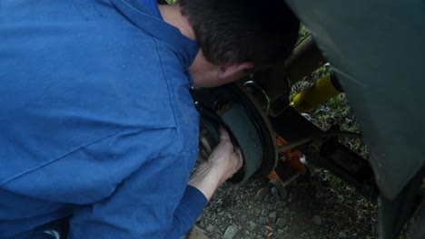 Mechanic-in-blue-coveralls-repairing-brakes-of-vehicle-outdoors,-changing-brake-pads