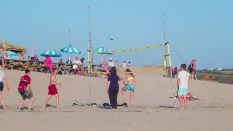 People-Playing-Volleyball-At-Beach-In-Summer,-Athletic-Woman-Jumps-And-Spikes-The-Ball-Over-The-Net