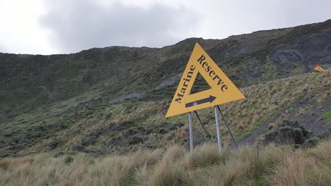 A-large-yellow-triangle-marine-reserve-sign-on-wild-rugged-coastline-on-the-South-Coast-in-Wellington,-New-Zealand-Aotearoa