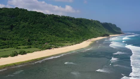 Breite-Luftaufnahme-Der-Küste-Von-Uluwatu-Auf-Bali-An-Einem-Sonnigen-Tag-Mit-Wellen,-Die-Am-Strand-Krachen,-Luftaufnahme