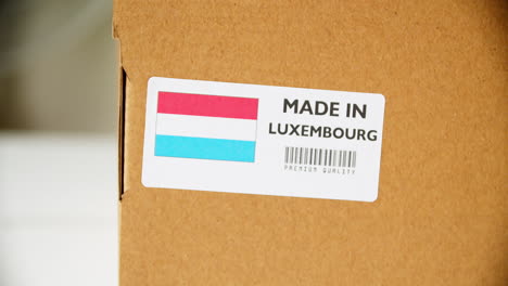 Hands-applying-MADE-IN-LUXEMBOURG-flag-label-on-a-shipping-cardboard-box-with-products