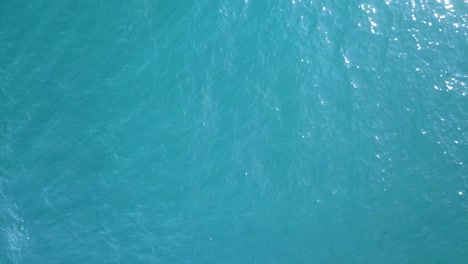 Aerial-top-down-view-of-fresh-and-beautiful-turquoise-blue-ocean-water-with-the-sun-reflections
