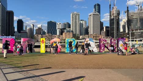 Happy-people-having-fun-climbing-up-block-sign-of-Brisbane-and-taking-photos-of-famous-urban-landmark-with-modern-downtown-cityscape-in-the-background-on-a-sunny-day,-Queensland,-Australia