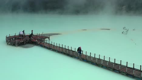people-walking-on-extreme-bridge-in-sulfur-lake-at-Kawah-Putih-in-Bandung,-aerial