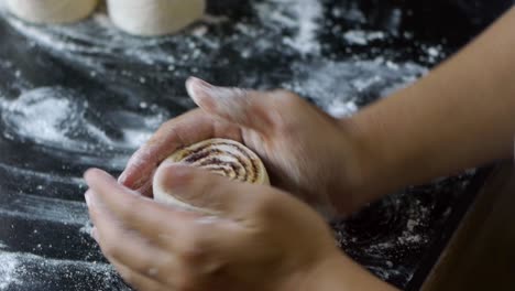 Freshly-cut-cinnamon-roll-being-shaped-with-dry-flour-using-fingers-on-kitchen-table-top-filmed-as-extreme-close-up