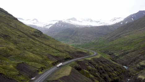 Ein-Sattelschlepper-Fährt-Durch-Die-Berge-Islands,-Während-Sich-Ein-Drohnenvideo-Dahinter-Bewegt