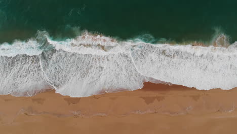 Horizontale-Luftaufnahme-Von-Oben-Nach-Unten-Auf-Den-Wunderschönen-Sandstrand,-Das-Grüne-Wasser-Des-Ozeans-Und-Die-Wellen,-Die-Am-Meeresufer-Krachen,-Entspannende-Meereslandschaft