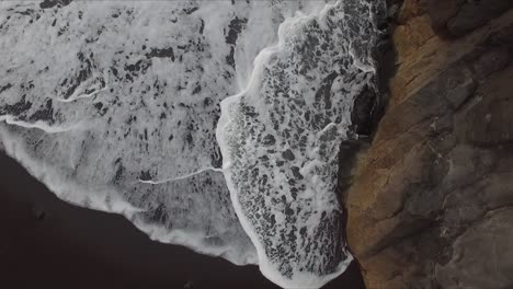 Aerial-view-of-splashes-and-swashes-of-waves-on-cliff-rocks-at-volcanic-beach-seashore