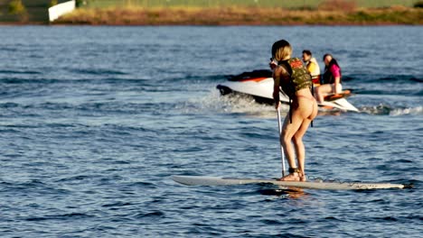 Mujer-En-Un-Paddleboard-Mientras-Un-Jet-Ski-Acelera-En-El-Lago-Paranoa
