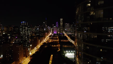 Drohne-Fliegt-Nachts-Rückwärts-Durch-Wolkenkratzer-In-Chicago-Mit-Der-Skyline-Im-Hintergrund