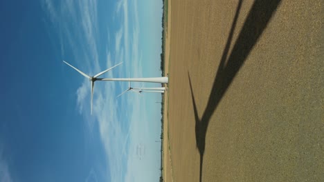 Sombra-De-Vídeo-Vertical-De-Una-Turbina-Eólica-Giratoria-En-Un-Campo-En-Un-Día-Soleado