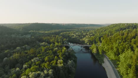 An-aerial-view-A-sunny-summer-evening-The-Gauja-river-flows-between-green-forests-and-a-bridge-crosses-the-river