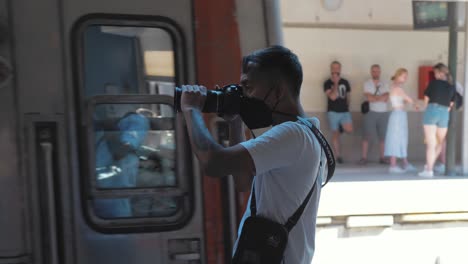 Young-male-filmmaker-filming-while-train-and-people-pass-by