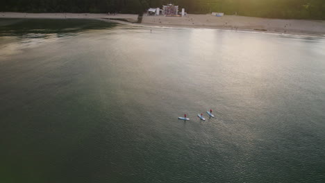 Aerial---people-oaring-standing-on-Paddleboards-in-Baltic-sea-by-the-Gdynia-public-beach-at-sunset