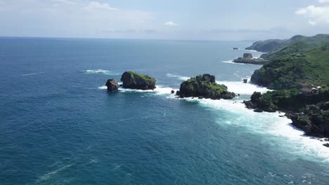 Drone-shot-of-rock-islands-on-the-beach,hit-by-waves-during-sunny-day---TIMANG-ISLAND,-YOGYAKARTA,-INDONESIA