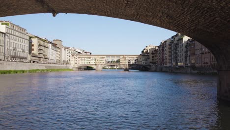 Ponte-Vechhio-Desde-El-Río-Arno,-Vuelo-Hacia-Atrás-Bajo-El-Puente-De-La-Santísima-Trinidad