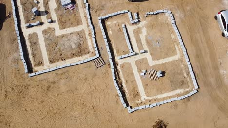Ascending-rotating-aerial-view-of-the-marked-out-housing-foundations-on-a-building-site,-showing-the-clearly-defined-footprint-of-the-house-to-be-built