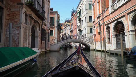 Vintage-Gondola-Sailing-On-Narrow-Canal-Towards-Venice-Bridge-In-Italy
