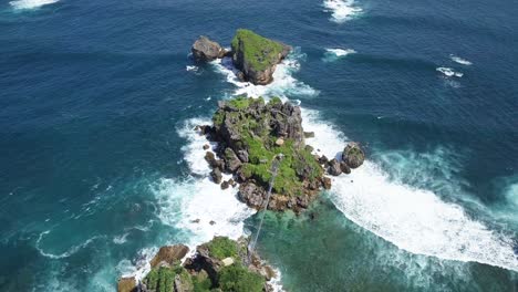 Aerial-view-of-overgrown-rocks-in-ocean,hit-by-waves-during-sunny-day---TIMANG-ISLAND,-YOGYAKARTA,-INDONESIA