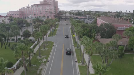 Luxury-cars-on-palm-tree-lined-road-near-Don-CeSar-Hotel,-St-Pete-Beach,-Florida