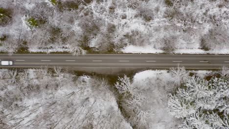 Winter-country-road-with-the-view-from-above,-fast-driving-cars-passing-by-the-straight-street,-top-shot-drone-view