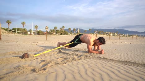 shirtless-muscular-guy-doing-planks-on-elbows-crawling-through-sand
