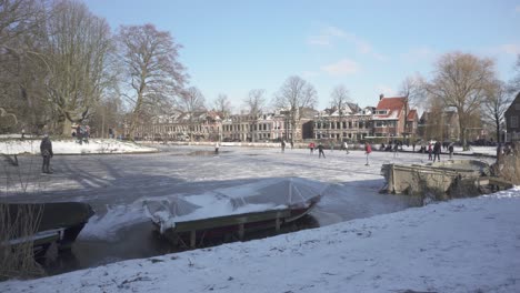 Dutch-locals-ice-skating-on-frozen-river-in-old-town,-traditional-winter-scene