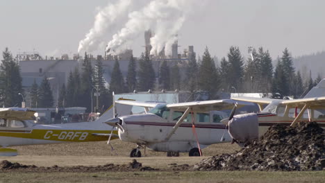 Aviones-Ligeros-Con-Planta-Industrial-En-Segundo-Plano-En-El-Aeropuerto-De-Quesnel,-Columbia-Británica,-Canadá