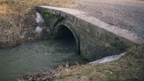 Slow-pan-of-water-flowing-fast-out-of-stone-sewage-system-outdoors