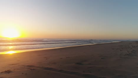 Drohne-Fliegt-Tief-Am-Strandufer-Entlang,-Während-Surfer-Herauslaufen,-Um-Eine-Welle-Zu-Fangen,-Mit-Einem-Wunderschönen-Sonnenaufgang-Im-Hintergrund-An-Der-Southport-Gold-Coast-QLD-Australien