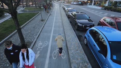 Aerial-view-of-kid-having-fun-riding-scooter-along-Arona-waterfront-bicycle-lane,-Italy