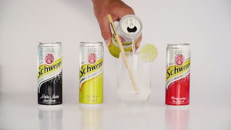 Hand-pouring-beverage-into-glass-with-bamboo-straw-lined-up-with-other-cans