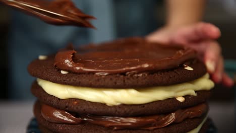 Spreading-chocolate-frosting-on-a-multi-layered-cake-filled-with-cream