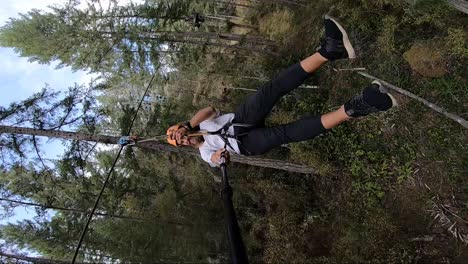 Vertical-action-camera-shot-of-a-young-man-sitting-with-legs-out-as-he-goes-down-the-zipline-very-fast