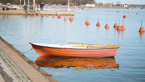Small-wooden-rowboat-with-oars-floating-on-the-water-while-anchored-in-the-dock