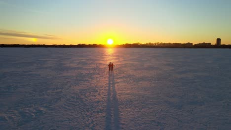 Couple-walking-over-a-frozen-lake-in-Minnesota-during-winter-time-during-a-beautiful-sunset,-travel-explore-only-in-mn