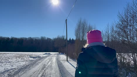 Mujer-Camina-Por-Un-Camino-Nevado-En-Un-Día-Soleado-Con-Fondo-Forestal-En-Invierno