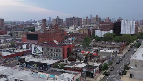 Aerial-rise-over-the-industrial-Bushwick-neighborhood-of-Brooklyn,-New-York-revealing-the-Manhattan-skyline-in-the-distance