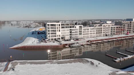 Noorderhaven-aerial-descend-and-approach-of-contemporary-new-luxury-apartment-building-in-bright-snow-cityscape-mirrored-in-the-high-water-level-in-the-recreational-port-in-the-foreground