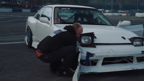Man-making-repairs-on-a-damaged-drift-car,-wide-shot-dolly-right