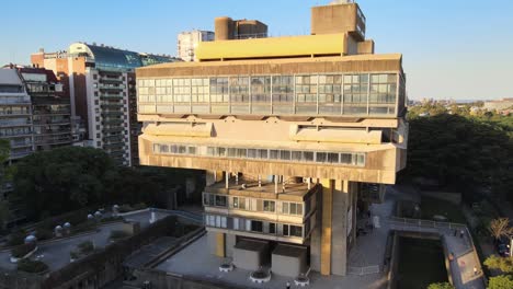 Aerial-dolly-out-of-Buenos-Aires-brutalist-style-National-Library-surrounded-by-buildings-and-trees-at-sunset