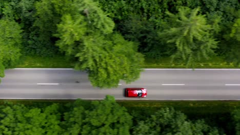 Fast-driving-red-car-driving-through-a-green-forest,-atracked-straight-from-above-as-a-drone-top-down-shot