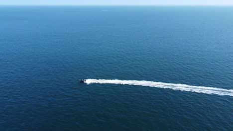 A-Fast-rigid-inflatable-boat-powers-across-the-frame-with-nothing-but-sea-and-horizon,-whilst-leaving-a-long-trail-of-wake-and-wash-behind