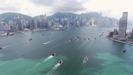 Konvoi-Lokaler-Fischerboote,-Die-In-Hongkong-Victoria-Bay-Verursachen,-Mit-Der-Skyline-Der-Stadt-Am-Horizont,-Luftbild