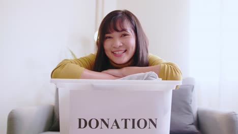 Retrato-De-Una-Joven-Asiática-Mirando-Una-Cámara-Sosteniendo-Una-Caja-Con-Ropa-Para-Donar