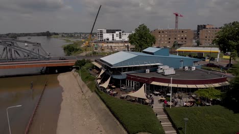 Aerial-sideways-rotating-pan-showing-IJsselpaviljoen-restaurant-and-corporate-venue-at-the-river-IJssel-with-people-on-the-terrace-during-high-water-level