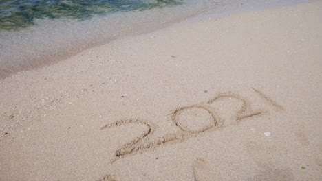 Die-Schrift-2021-Auf-Dem-Weißen-Sand-Des-Strandes-Verliert-Sich-In-Den-Wellen