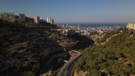 View-over-a-winding-road-between-the-hills-with-the-port-city-of-Haifa-in-the-early-evening,-horziont-with-the-sea-and-boats,-Israel